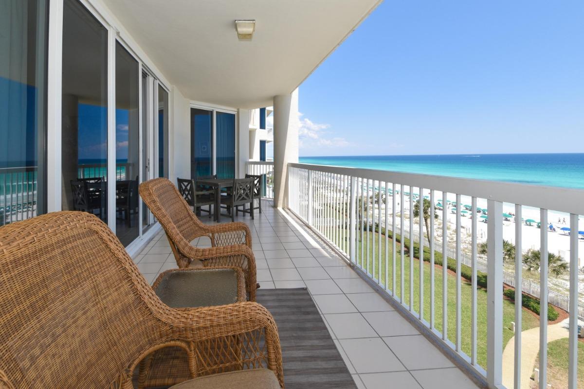 The spacious balcony of a beachfront vacation rental in Destin, Florida, with a sweeping view of the crystal-clear turquoise sea and white sandy beach lined with umbrellas.