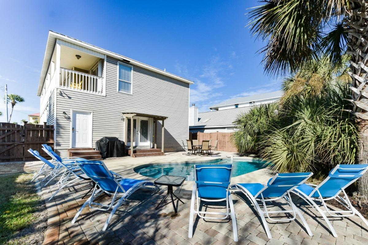 A two-story vacation rental home in Destin, Florida, with light gray siding and white trim, featuring a private pool.
