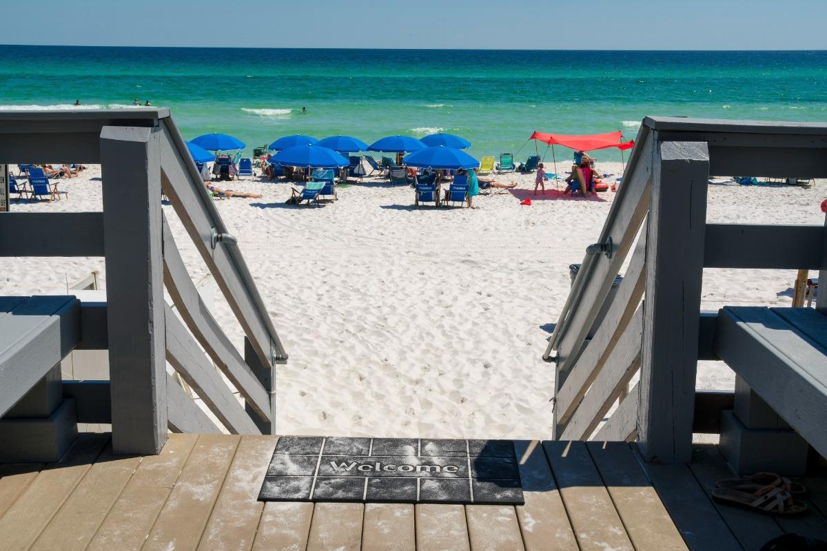 View from a deck leading to the white sand and emerald waters near Okaloosa Island condos, with beach chairs and umbrellas set up along the shore.